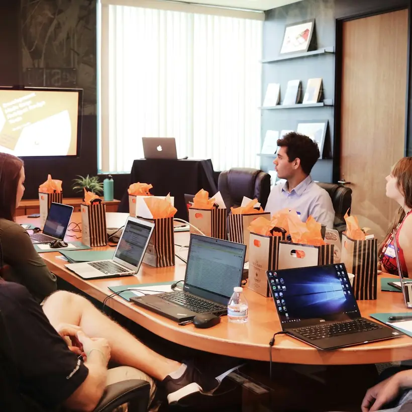Reunión de equipo alrededor de una mesa con varios portátiles abiertos