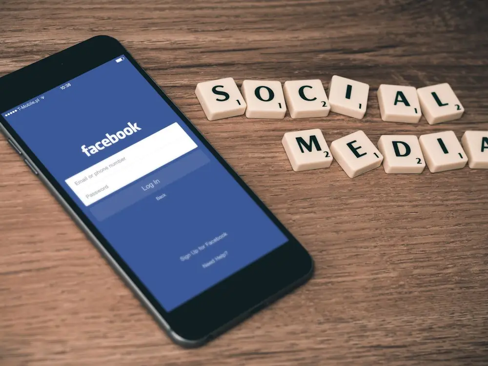 Teléfono móvil con la aplicación de Facebook junto a fichas que forman la palabra social media